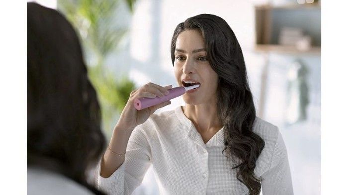 Photo of woman brushing her teeth with pinkelectric toothbrush.